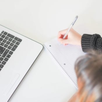 Photo of a woman writing a condo checklist in a notebook by her laptop.