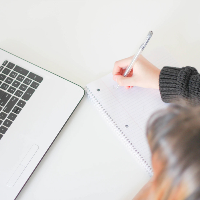 Photo of a woman writing a condo checklist in a notebook by her laptop.