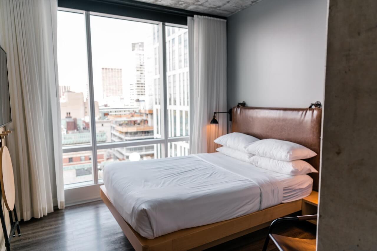 A white linen on the bed near the glass window with a view photo by Andrea Davis